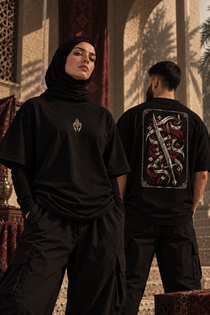 Two models wearing WAQT Khalid bin Waleed Undefeated T-shirts in a courtyard